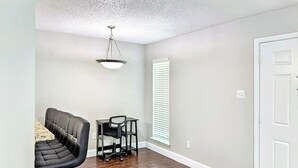 Une pièce avec un plancher en bois foncé, un fauteuil en cuir noir, une petite table et une porte blanche.
