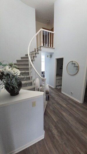 A staircase leading to an upper level, a round mirror on the wall, and a potted plant on a counter. - Cutie On The Corner (Omaha)