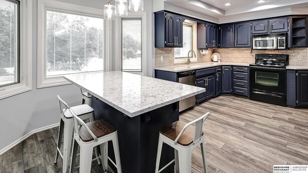 A modern kitchen with dark cabinets, a granite countertop, and a central island with bar stools. - Cutie On The Corner (Omaha)
