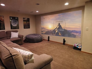 Una sala de estar con un sofá marrón, un sillón tipo flex y un gran mural en la pared que muestra un paisaje montañoso.