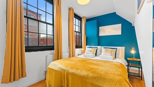 Ein Schlafzimmer mit einem Bett, Vorhängen, einem Nachttisch, einer Lampe und einem Bild an der Wand.