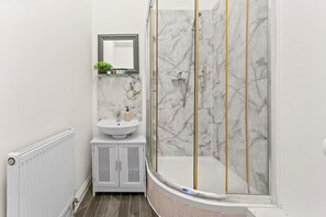 Une salle de bain avec un lavabo en marbre blanc, un miroir, une douche avec des portes en verre et un radiateur.