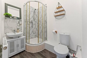 Et badeværelse med bruseniche, toilet, vask og spejl.