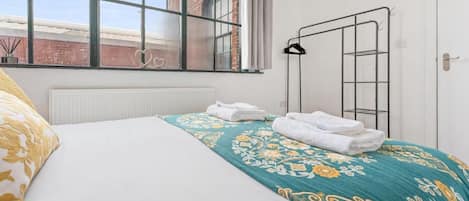 Une chambre d’hôtel avec un lit, une fenêtre donnant sur un immeuble en briques, un radiateur et un porte-serviettes.