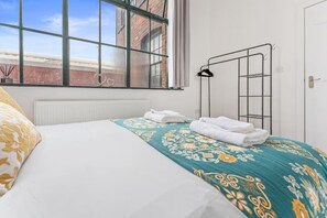 Et hotelværelse med en seng, et vindue med udsigt til en murstensbygning, en radiator og et håndklædestativ.