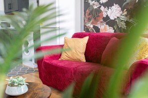 Un canapé rouge avec un coussin beige, dans une pièce où se trouvent un lave-linge et une plante en pot.