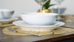 Une table à manger avec un bol blanc, une fourchette, un verre et une nappe décorée de motifs dorés.