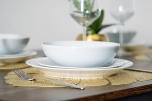 Une table à manger avec un bol blanc, une fourchette, un verre et une nappe décorée de motifs dorés.