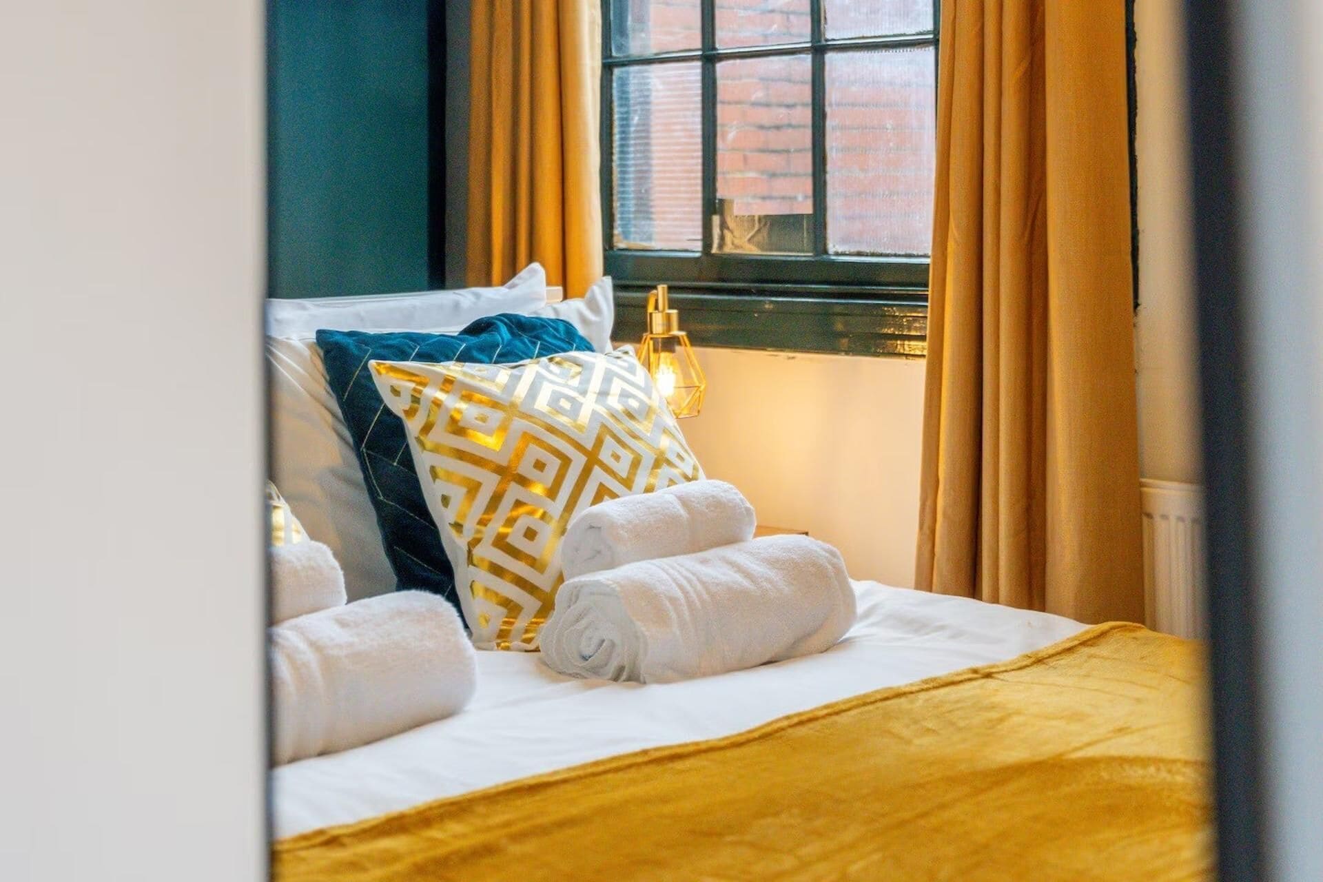 A neatly made bed with white linens, a yellow throw blanket, and patterned pillows.