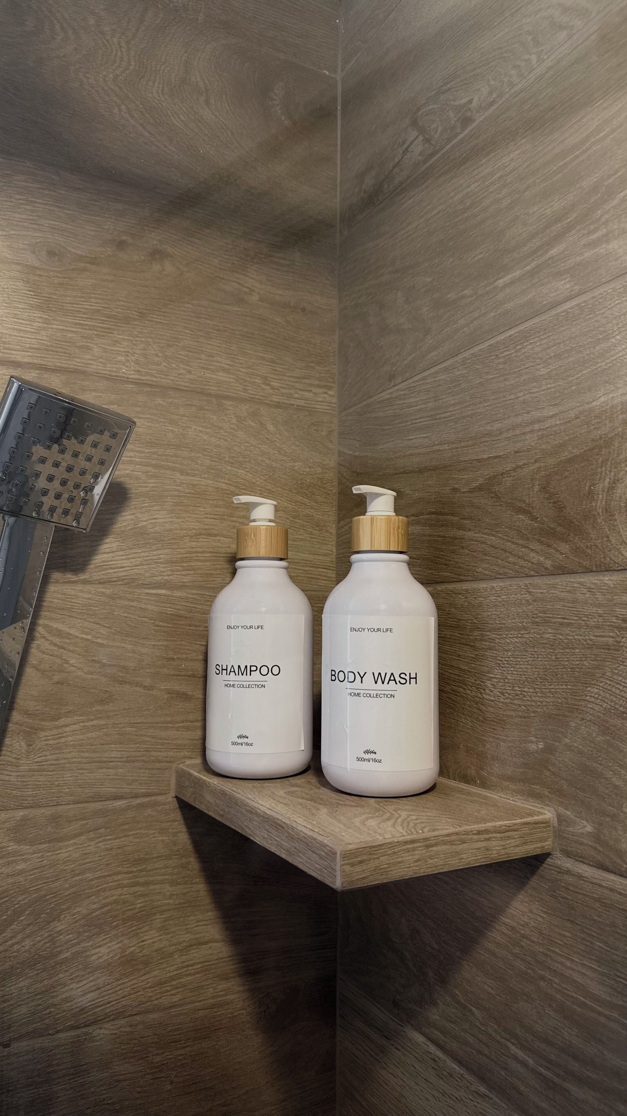 Two white bottles of shampoo and body wash on a wooden shelf in a bathroom.