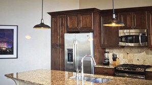 Una cocina con encimeras de granito, electrodomésticos de acero inoxidable, gabinetes de madera oscura e iluminación colgante.