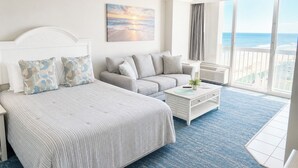 Une chambre d’hôtel avec un lit, un canapé, une table basse et une grande fenêtre donnant sur l’océan.