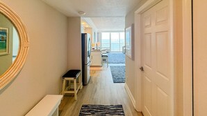 A hallway with a wooden floor, a small table, a refrigerator, and a door leading to a balcony. - The Reserve | Oceanfront Studio | Private Balcony (Daytona Beach)
