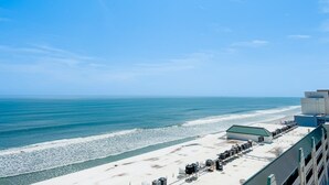 Vista de la playa con un edificio que tiene una larga hilera de unidades de aire acondicionado y un área cubierta con techo verde.