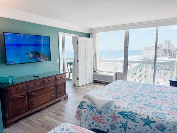 Un dormitorio con una cama grande, un televisor en la pared, un aparador y vistas al océano.