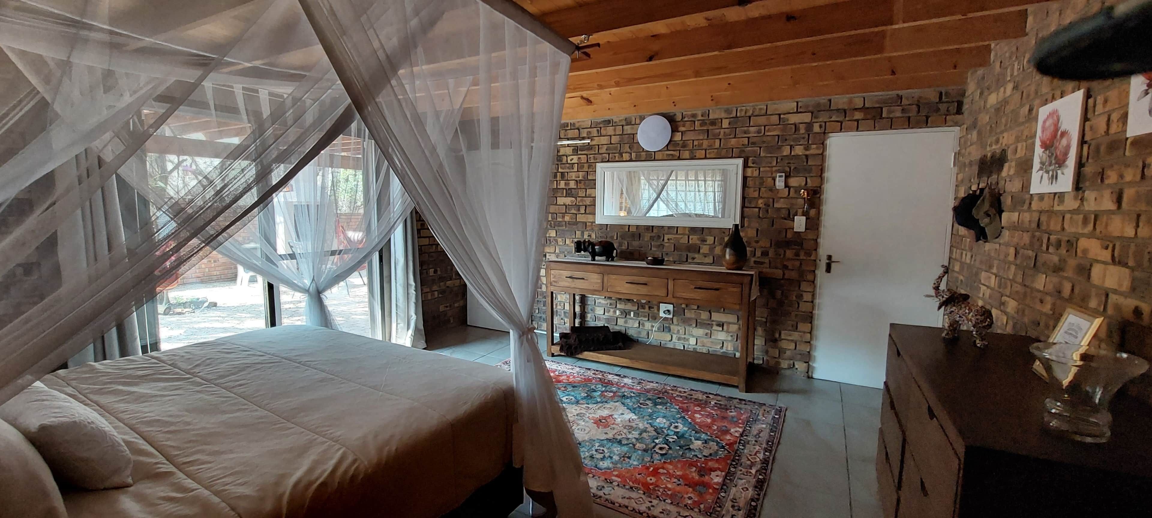 Un dormitorio con cama, mesita de noche, cómoda, espejo y pared de ladrillo.
