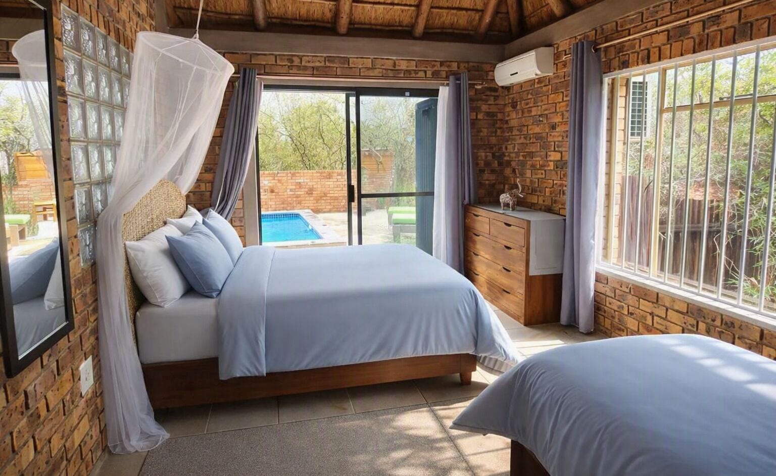 A bedroom with a bed, a nightstand, a window with curtains, a brick wall, and a view of a swimming pool.