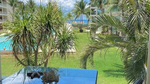 A view from a balcony overlooking a pool, palm trees, and a building with a clear sky.