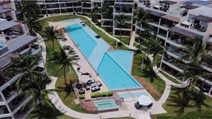 A resort with two large swimming pools, palm trees, and modern buildings.