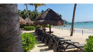 A beach with thatched umbrellas, lounge chairs, and a clear view of the ocean.