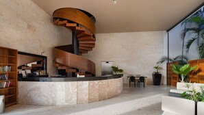 A modern interior with a spiral staircase, a reception desk, a seating area, and a large window with plants.