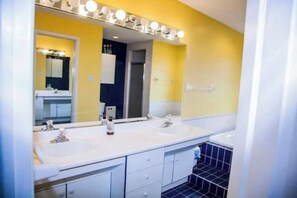 A bathroom with two sinks, a large mirror with lights, and a tiled floor.