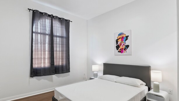 A neatly arranged bedroom with a bed, two bedside tables with lamps, a wall-mounted artwork, and a window with curtains. - Lovely 3bed 2bath apartment near Universal studio & Hollywood in Los Angeles (Los Angeles)