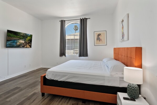 Une chambre à coucher avec un lit, une table de chevet, une lampe et des œuvres d’art accrochées aux murs.