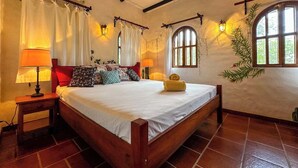 A bedroom with a wooden bed, two bedside lamps, a window with curtains, and a wall-mounted light fixture.