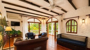 A spacious living area with a high ceiling, large windows, and a balcony.