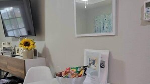 A modern room with a flat-screen TV, a ceiling fan, a white table with a bowl of snacks, and a white chair. - Northgate Studio - 1 block from TAMU! (College Station)