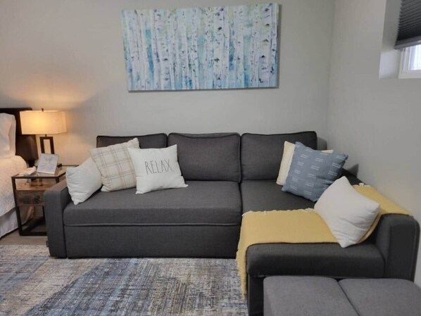 A modern living room with a grey sectional sofa, a small side table, a lamp, and a painting on the wall.