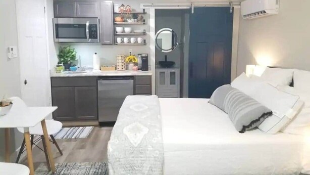 A compact hotel room with a kitchenette, a bed with pillows, a small table, and a mirror. - Northgate Studio - 1 block from TAMU! (College Station)