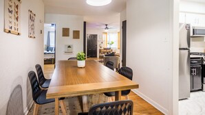 Een eethoek met een houten tafel en zwarte stoelen, een plafondventilator, en een keuken in de achtergrond.