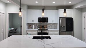 A modern kitchen with white cabinets, a marble island, stainless steel appliances, and pendant lighting.
