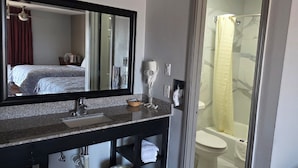 A bathroom with a granite countertop, a mirror, a hairdryer, a towel rack, and a shower enclosure.