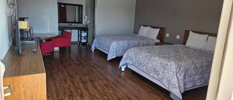 A hotel room with two beds, a desk with a chair, a mirror, and a microwave.