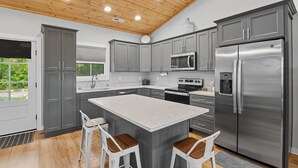 A modern kitchen with grey cabinets, stainless steel appliances, and a wooden ceiling.