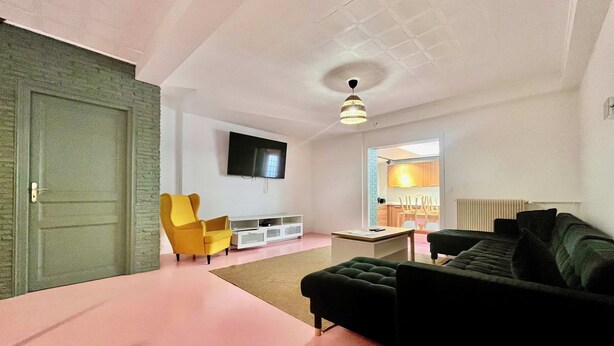 Una sala de estar moderna con un televisor de pantalla plana, un sillón amarillo, un sofá negro y una pequeña mesa de centro.