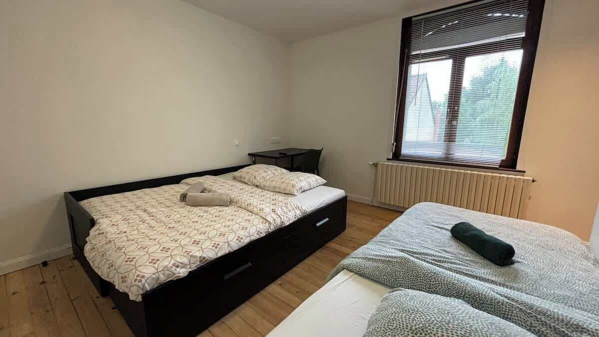 Un dormitorio con cama, una mesita y una ventana con persianas.