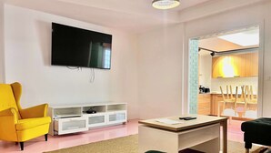 Una sala de estar moderna con un televisor de pantalla plana, un sillón amarillo, un sofá verde oscuro y una pequeña mesa de centro.