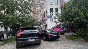 Un’area di parcheggio con due auto, un edificio con un cartello e un albero.