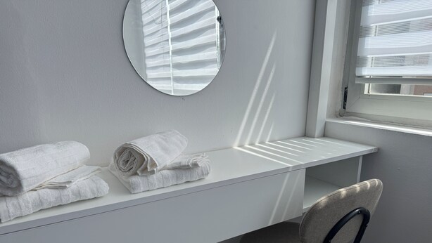 Un bagno con un mobile lavabo bianco, due asciugamani arrotolati, uno specchio e una sedia.