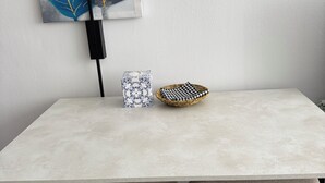 Un'area pranzo minimalista con un tavolo chiaro, due sedie imbottite, un cesto decorativo e un'opera d'arte incorniciata al muro.