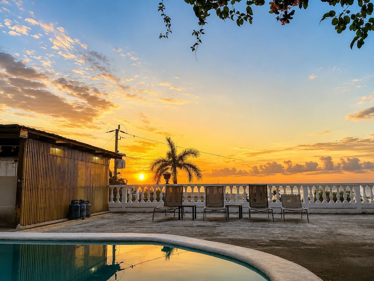 A poolside area with chairs, a building, and a sunset view.