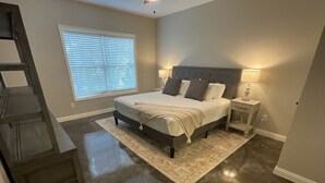 Un dormitorio con cama, mesitas de noche, lámpara, ventana con persianas y una escalera.