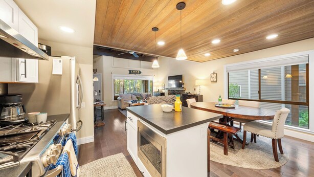 A modern kitchen with a central island, a dining area with a wooden table and chairs, and a living room with a sofa and fireplace. - Near Ski, Beach, & Hiking Trails + Clubhouse Pool & Hot Tub Access Juanita Blue by Avantstay (Incline Village)