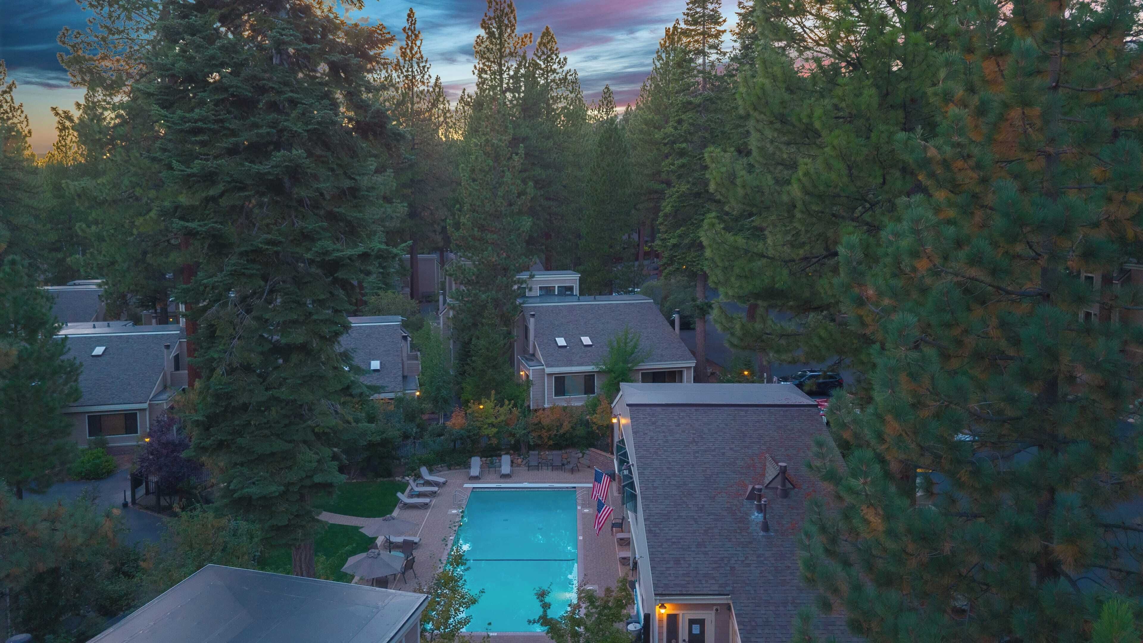 A residential area with a swimming pool surrounded by houses and dense trees.