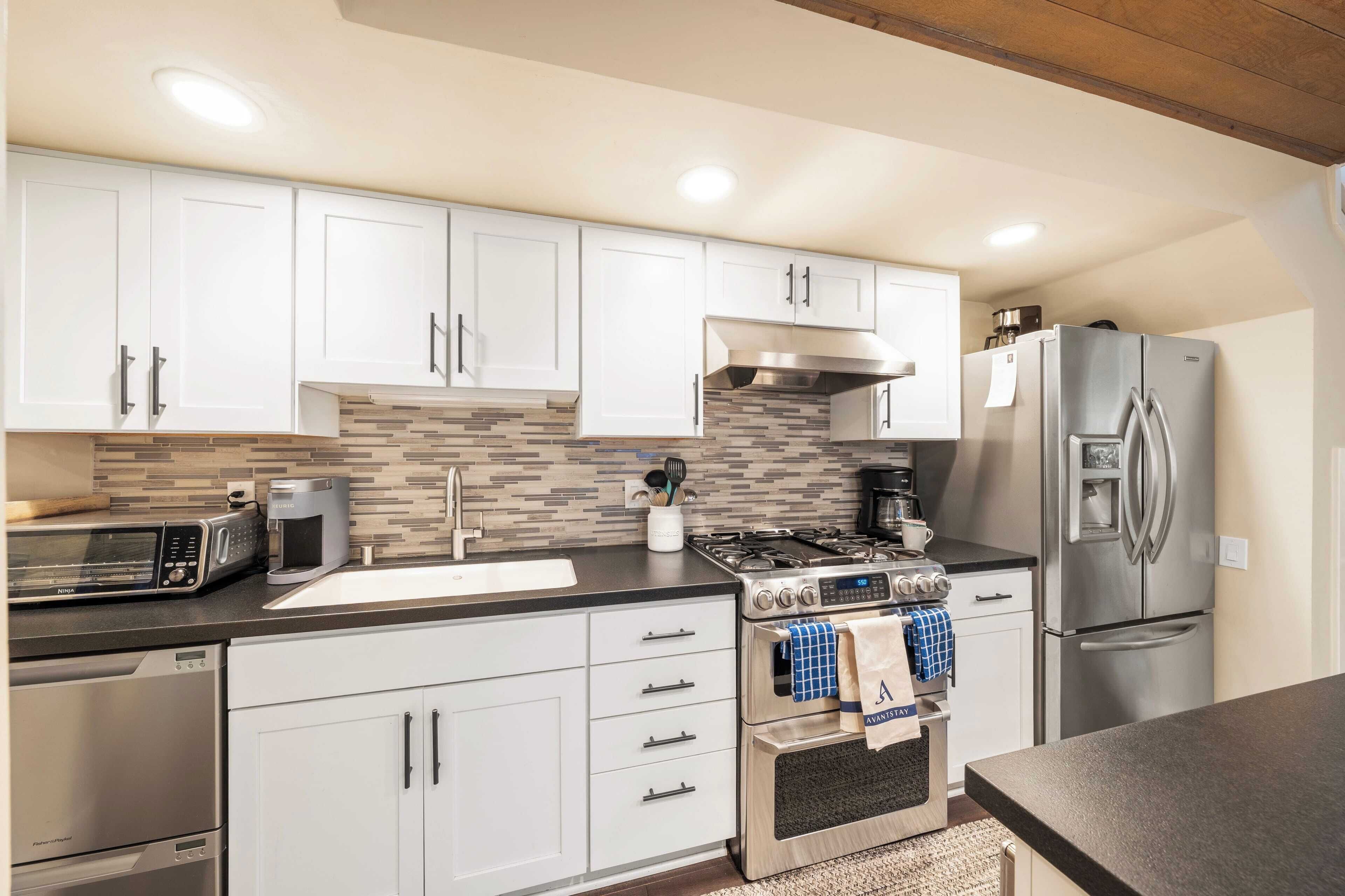Una cocina moderna con armarios blancos, un refrigerador de acero inoxidable, horno empotrado y cafetera.