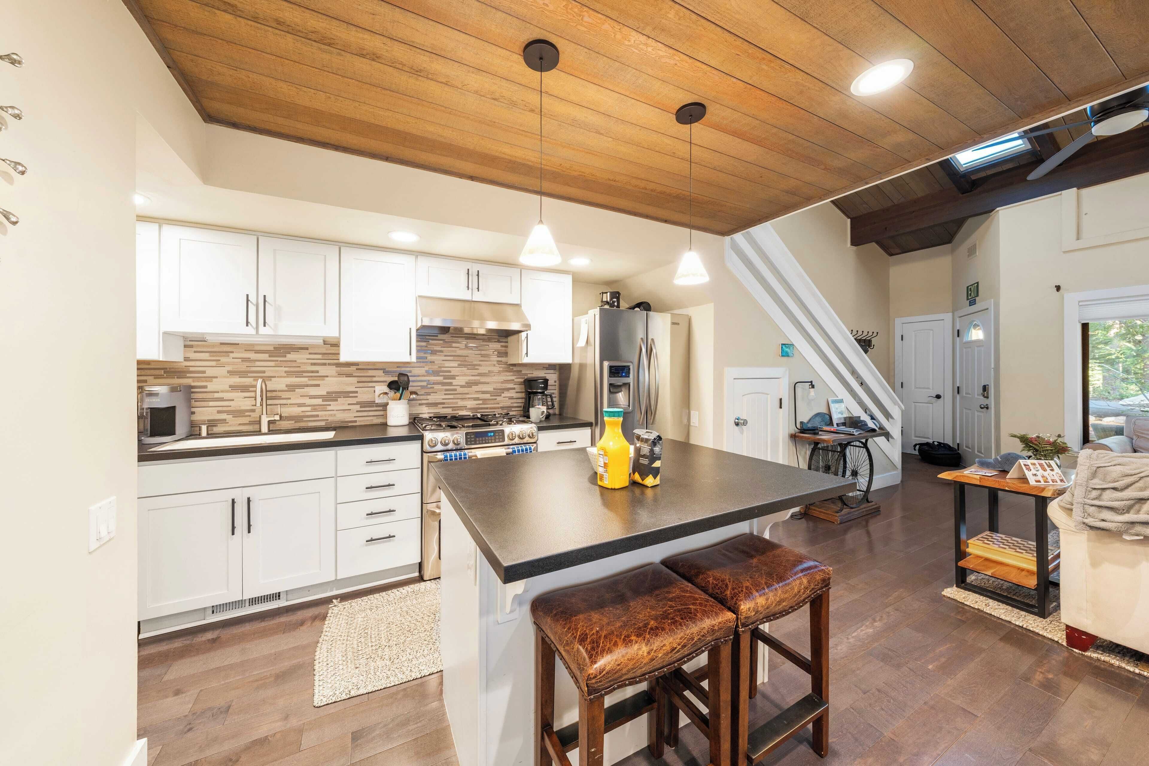 Una cocina moderna con armarios blancos, una isla grande con taburetes, una estufa y un refrigerador.